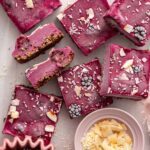 Frozen blackberry cobbler bars on a parchment-lined wire rack with fresh blackberries and shredded coconut