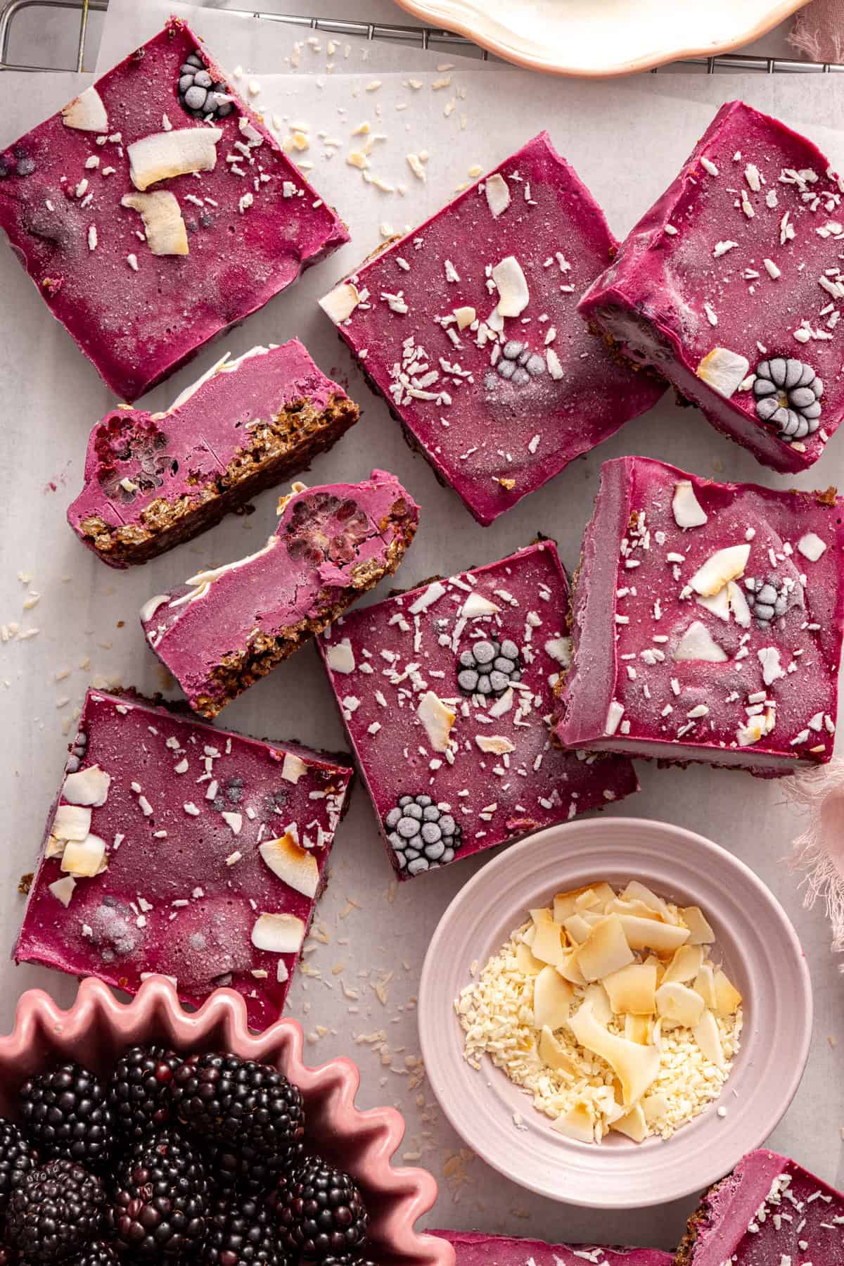 Frozen blackberry cobbler bars on a parchment-lined wire rack with fresh blackberries and shredded coconut