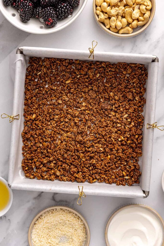 granola crust pressed into parchment-lined pan for blackberry cobbler bars