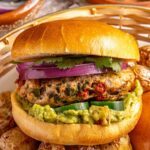 Homemade jalapeño burger with guacamole, cilantro and red onion in a bun served with roasted potatoes