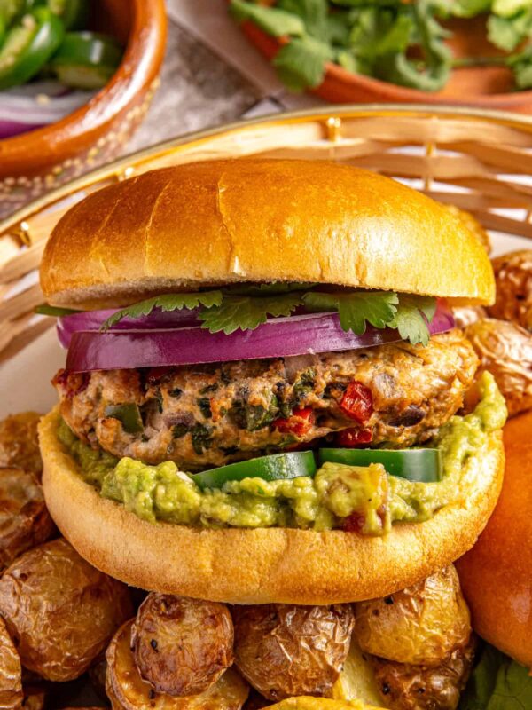 Homemade jalapeño burger with guacamole, cilantro and red onion in a bun served with roasted potatoes