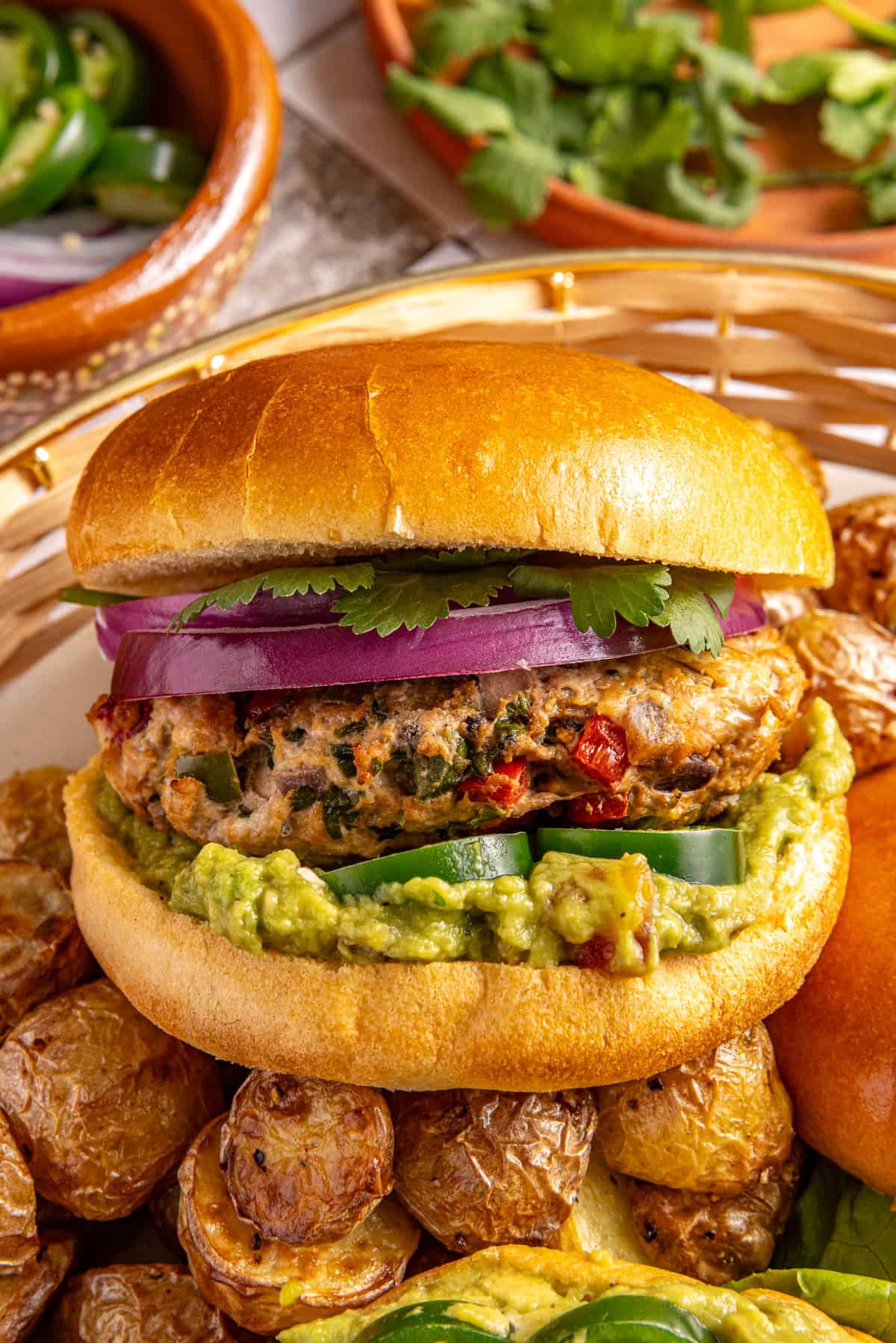 Homemade jalapeño burger with guacamole, cilantro and red onion in a bun served with roasted potatoes