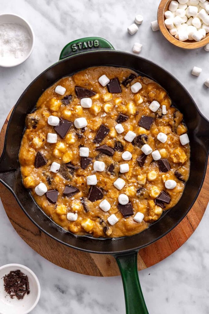 Topping gluten-free s'mores cookie skillet with chocolate and marshmallows