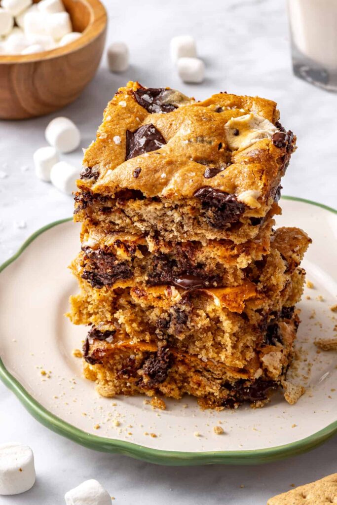 Stacked gluten-free s'mores cookie bars served on a plate with a glass of milk