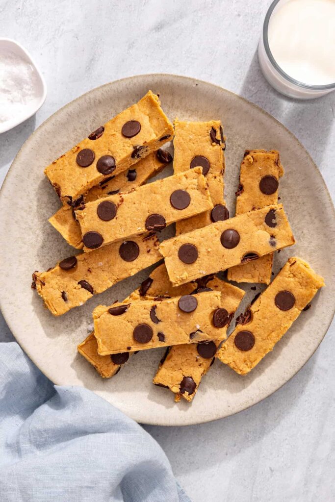 Chocolate chip peanut butter protein bars on serving plate next to glass of milk and cloth napkin