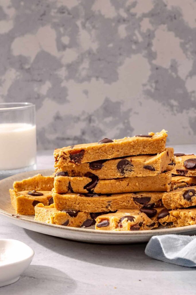 Stacked peanut butter protein bars on plate with glass of milk
