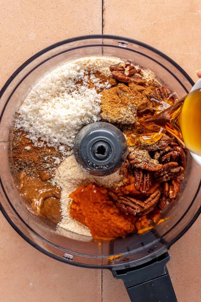 Ingredients in a food processor for pumpkin protein balls including pumpkin purée, pecans, and almond butter