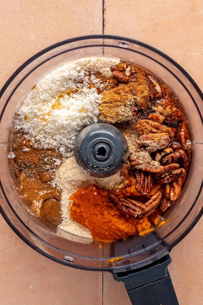 Ingredients in a food processor for pumpkin protein balls including pumpkin purée, pecans, and almond butter