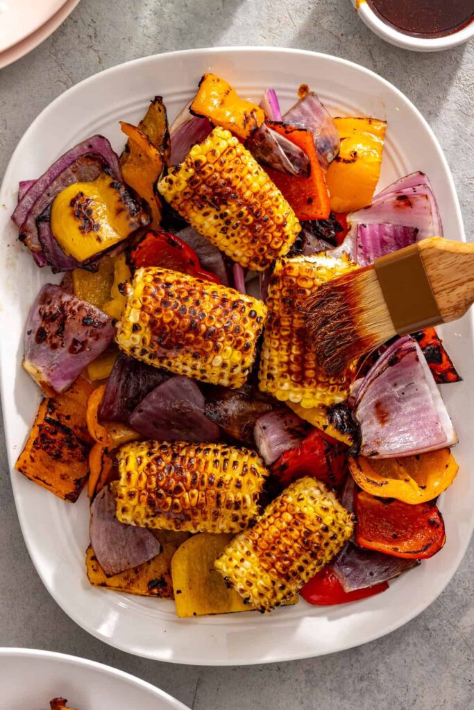 Brushing seasoned ghee onto grilled corn for grilled teriyaki chicken dinner