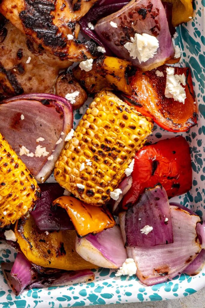 zoomed in shot of grilled corn and vegetables next to chicken teriyaki, served on a speckled platter