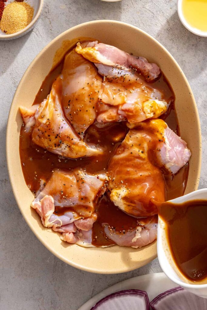 pouring teriyaki sauce over chicken thighs for a high-protein grilling recipe