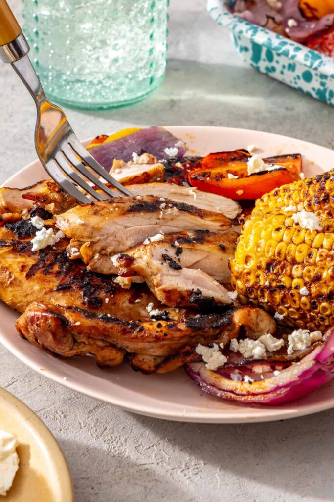 Fork lifting sliced grilled teriyaki chicken with grilled vegetables