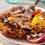 Close-up of sliced grilled teriyaki chicken served with grilled vegetables and corn on a dinner plate