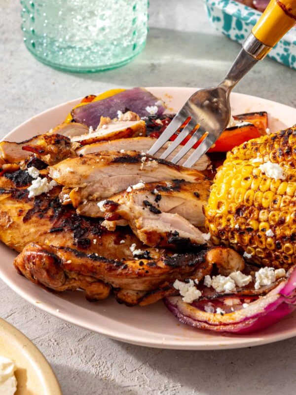 Close-up of sliced grilled teriyaki chicken served with grilled vegetables and corn on a dinner plate