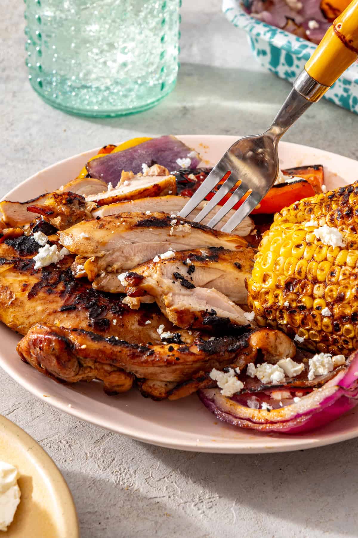 Close-up of sliced grilled teriyaki chicken served with grilled vegetables and corn on a dinner plate