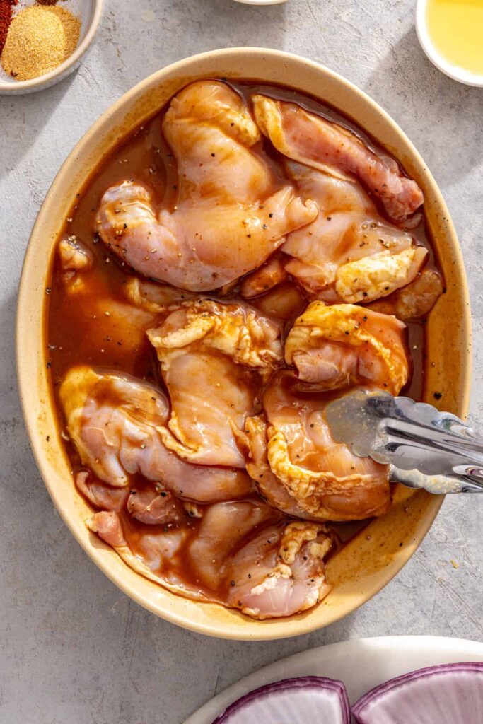 using tongs to nestle chicken thighs in teriyaki marinade