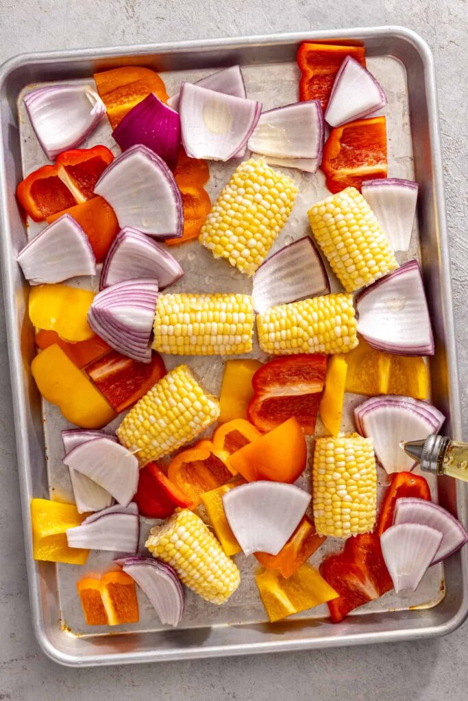 drizzling olive oil over corn, peppers, and onion for grilled teriyaki chicken dinner