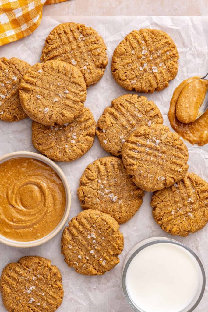 Gluten-free peanut butter cookies on a styled table with creamy peanut butter, a linen napkin and a glass of milk nearby