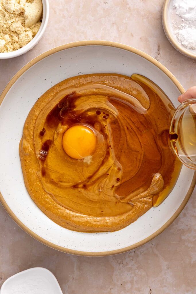 pouring melted and cooled coconut oil into peanut butter cookie dough batter