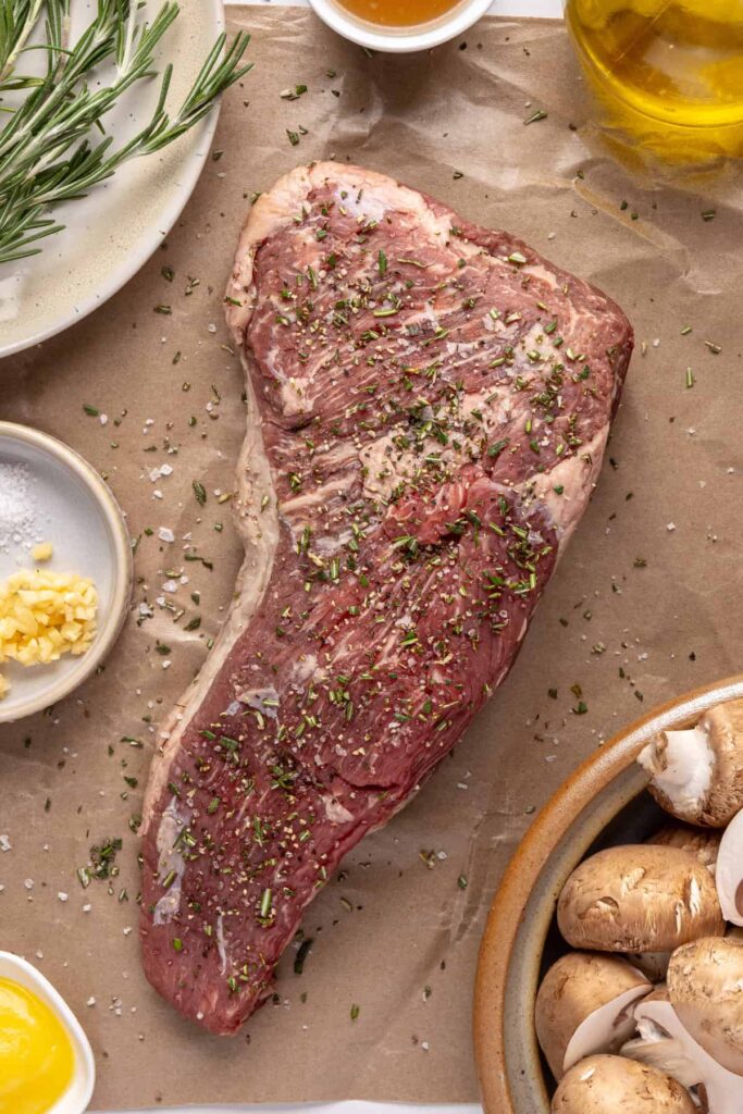 Juicy grass-fed tri-tip steak on a cutting board, seasoned with salt, pepper, and fresh rosemary