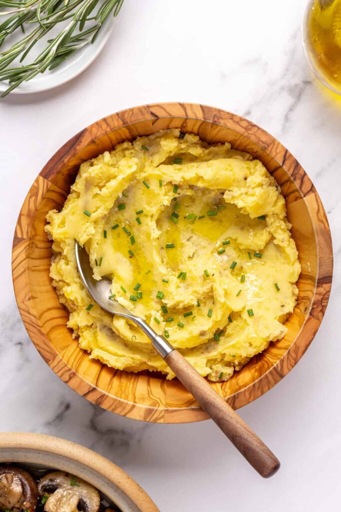 Creamy homemade mashed potatoes garnished with chopped chives, served in a wooden bowl