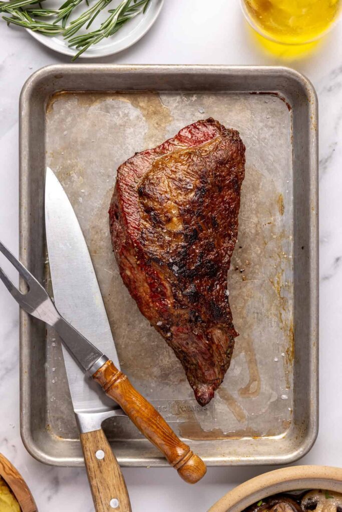 Juicy grass-fed tri-tip steak on a cutting board, seasoned with salt, pepper, and fresh rosemary