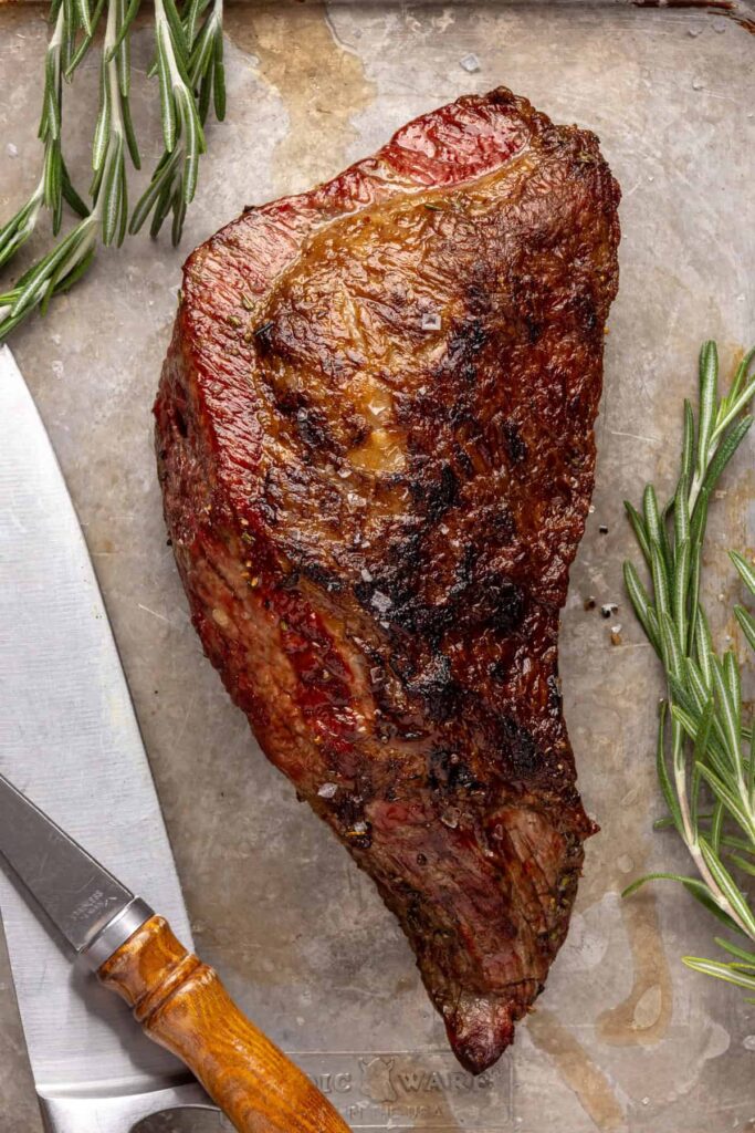 close-up of juicy grass-fed tri-tip steak on a cutting board, seasoned with salt, pepper, and fresh rosemary