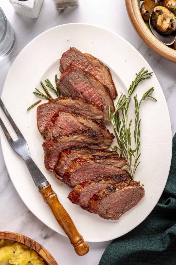 Sliced grilled tri-tip steak with rosemary and cracked black pepper, cooked medium-rare