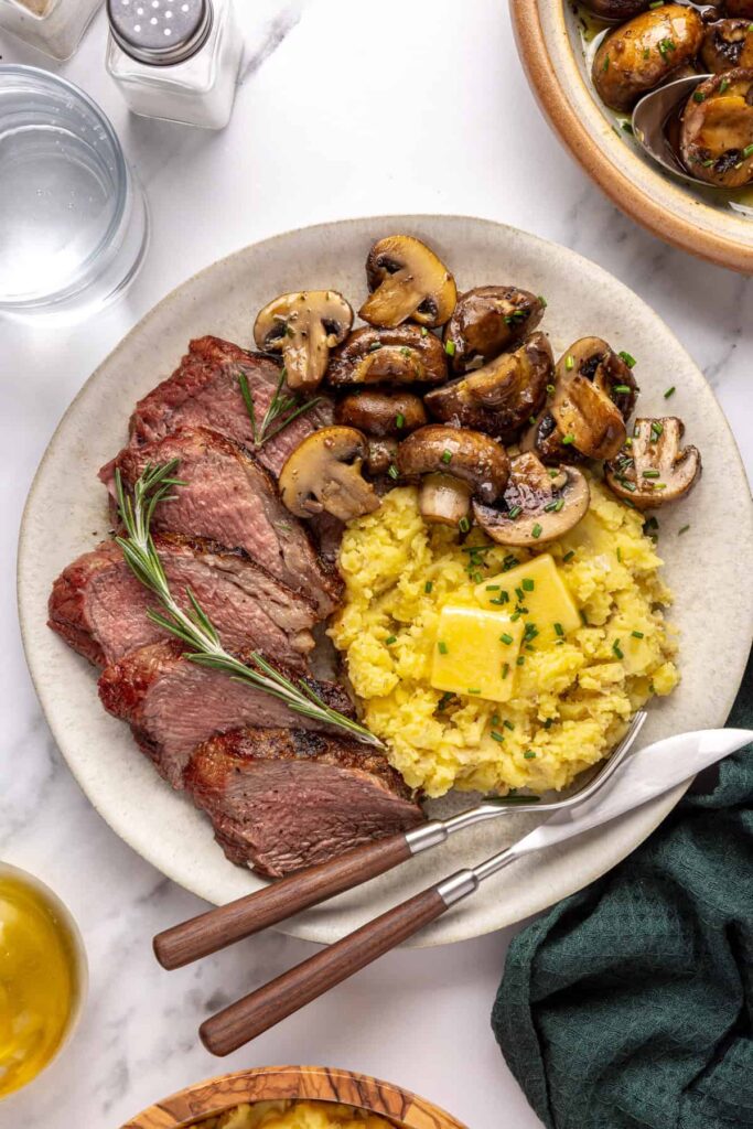 Tri-tip steak served with creamy mashed potatoes and garlicky mushrooms on a dinner plate