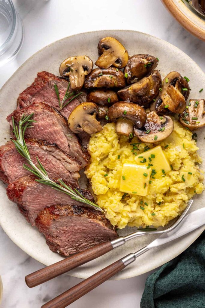 Steakhouse-style tri-tip steak dinner with mashed potatoes and sautéed garlic mushrooms, plated for serving