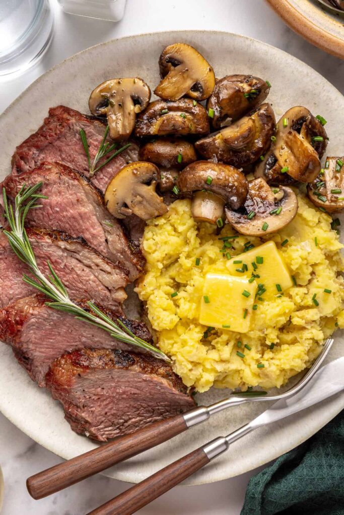 Steakhouse-style tri-tip steak dinner with mashed potatoes and sautéed garlic mushrooms, plated for serving
