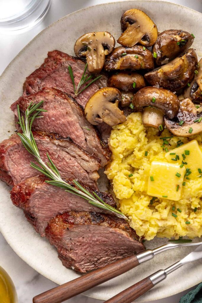 Steakhouse-style tri-tip steak dinner with mashed potatoes and sautéed garlic mushrooms, plated for serving