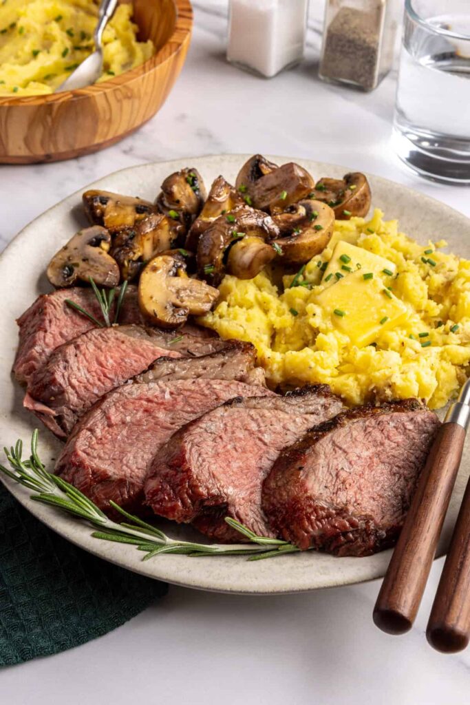 Steakhouse-style tri-tip steak dinner with mashed potatoes and sautéed garlic mushrooms, plated for serving