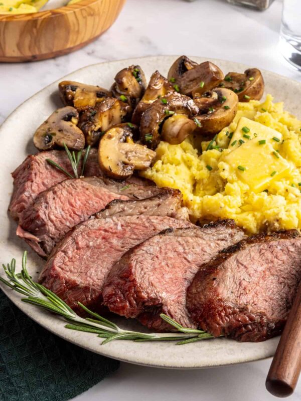 Tri-tip steak served with creamy mashed potatoes and garlicky sautéed mushrooms on a plate, steakhouse-style dinner
