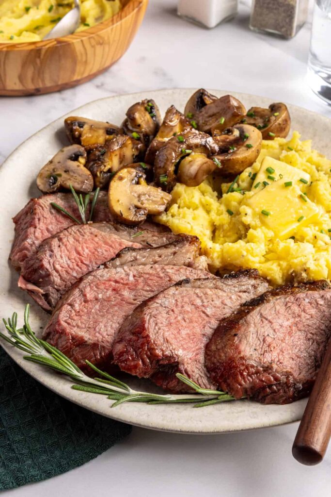 Tri-tip steak served with creamy mashed potatoes and garlicky sautéed mushrooms on a plate, steakhouse-style dinner
