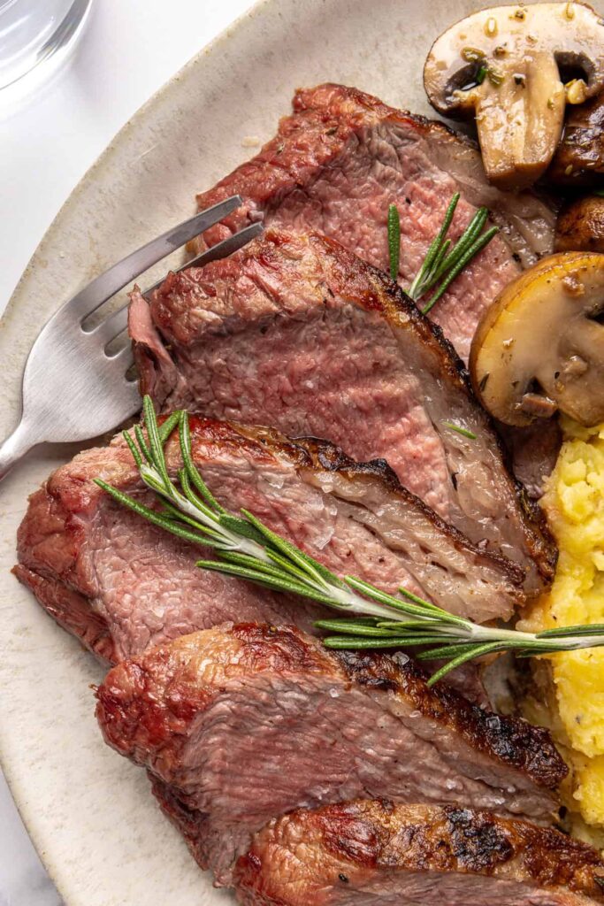 close-up of tri-tip steak served with creamy mashed potatoes and garlicky mushrooms on a dinner plate