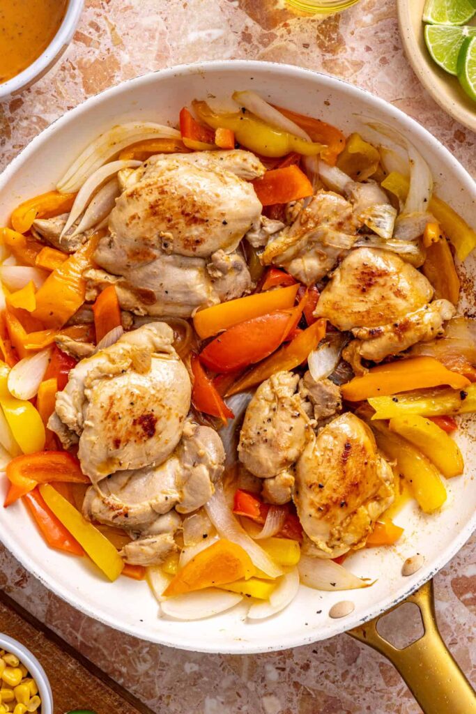Chicken thighs searing in skillet with peppers and onions