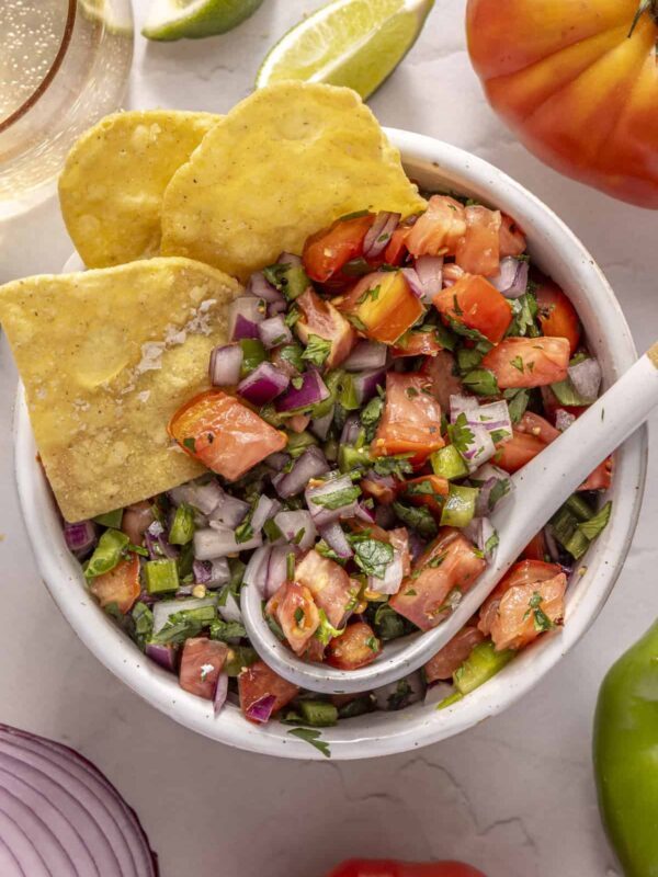 Scooping easy homemade pico de gallo with grain-free tortilla chips for a healthy snack