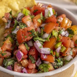 Scooping easy homemade pico de gallo with grain-free tortilla chips for a healthy snack