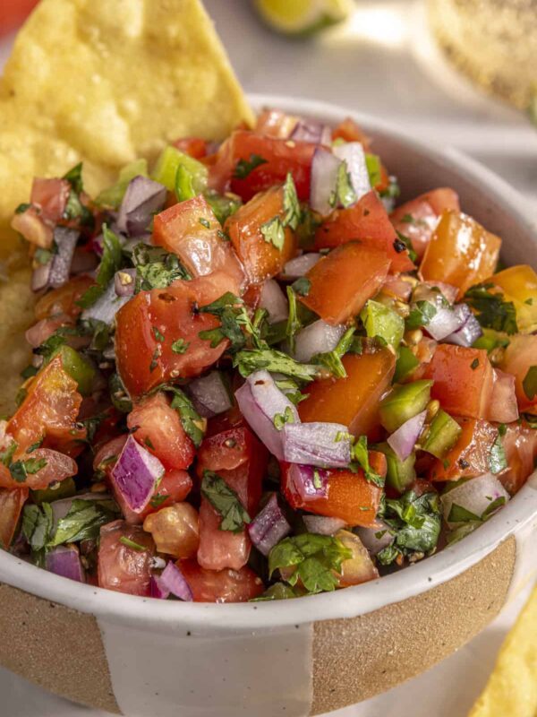Scooping easy homemade pico de gallo with grain-free tortilla chips for a healthy snack