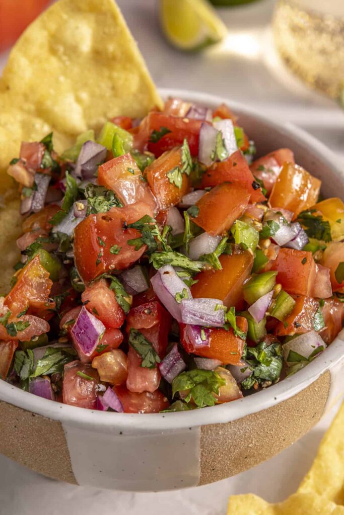 Scooping easy homemade pico de gallo with grain-free tortilla chips for a healthy snack