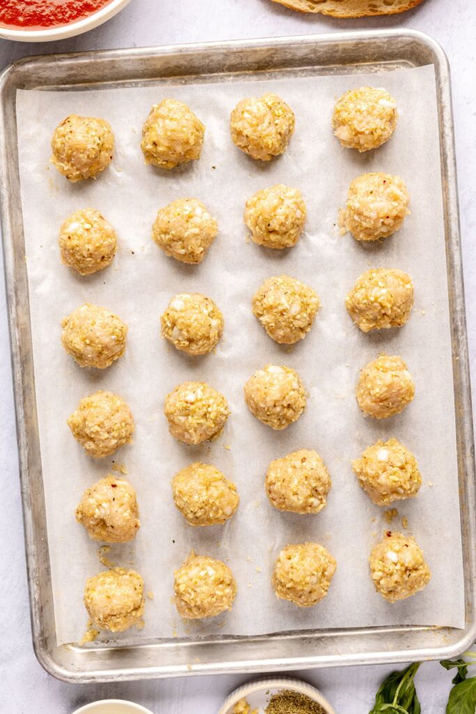 prepping chicken meatballs on a baking sheet before searing in a skillet