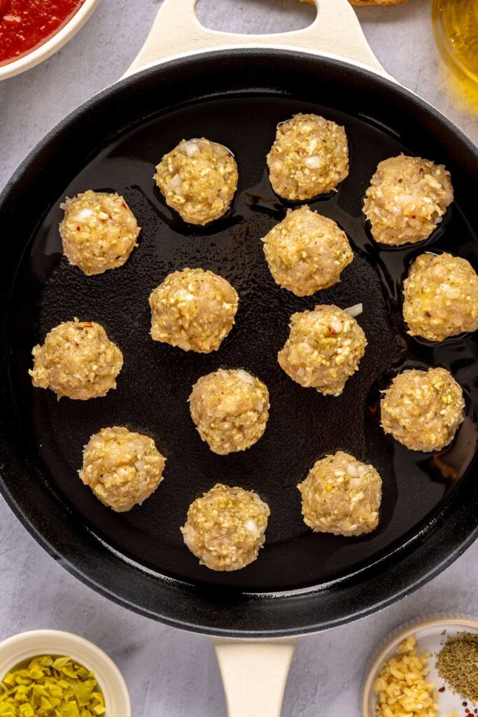 Searing golden chicken meatballs in a large skillet before simmering in sauce