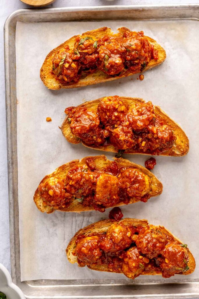 Open-faced, high-protein chicken pesto parmesan meatball subs with marinara sauce and melted cheese