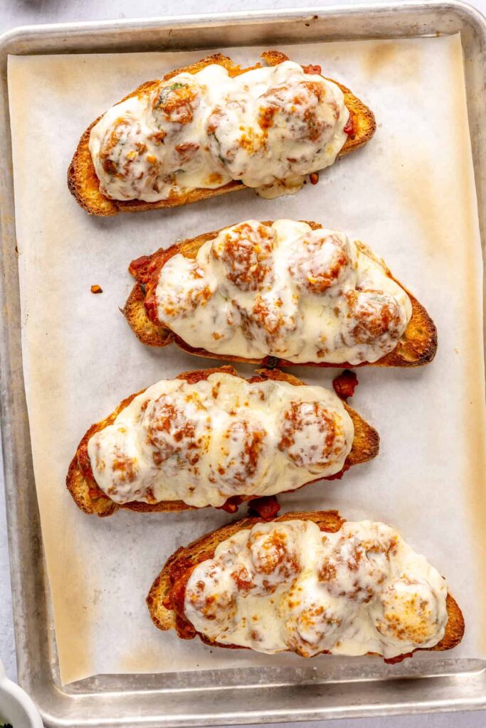 Open-faced, high-protein chicken pesto parmesan meatball subs with marinara sauce and melted cheese