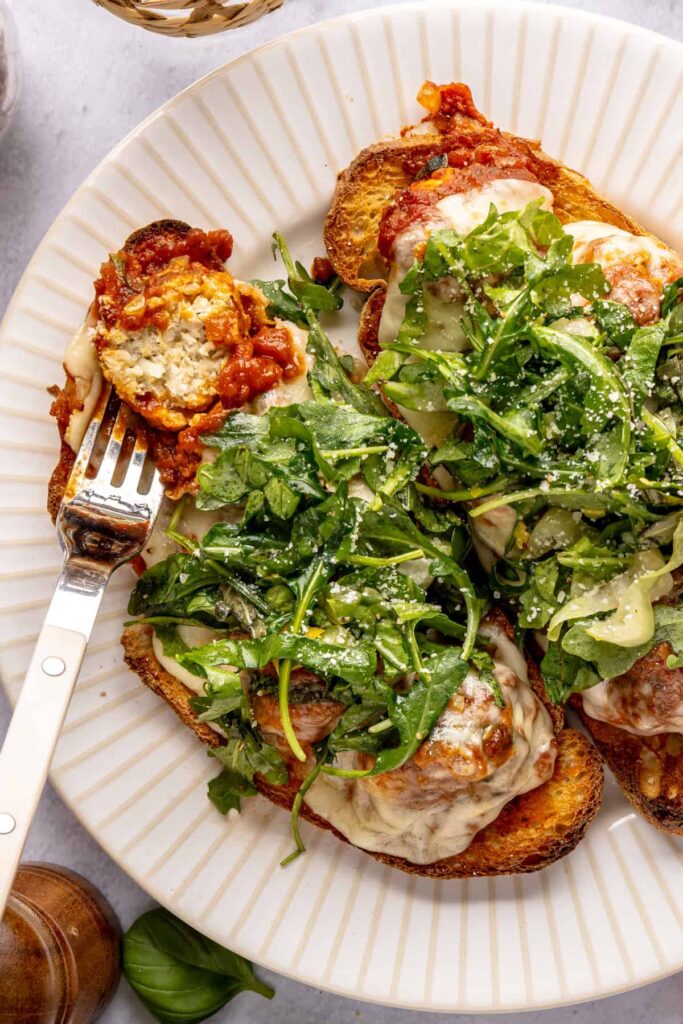 Open-faced, high-protein chicken pesto parmesan meatball subs with marinara sauce and melted cheese