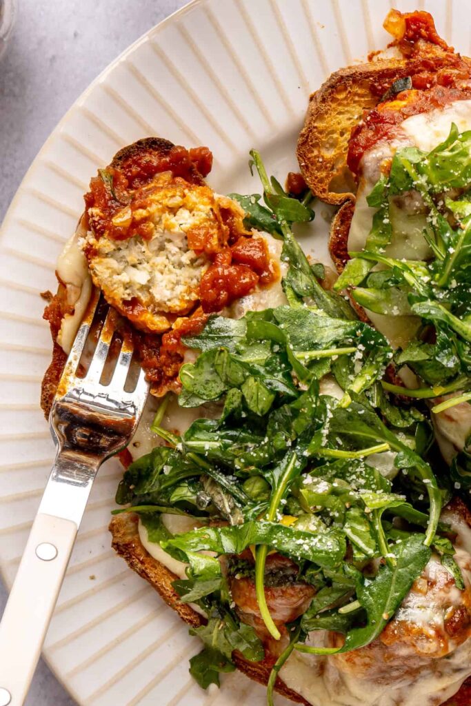 Open-faced, high-protein chicken pesto parmesan meatball subs with marinara sauce and melted cheese