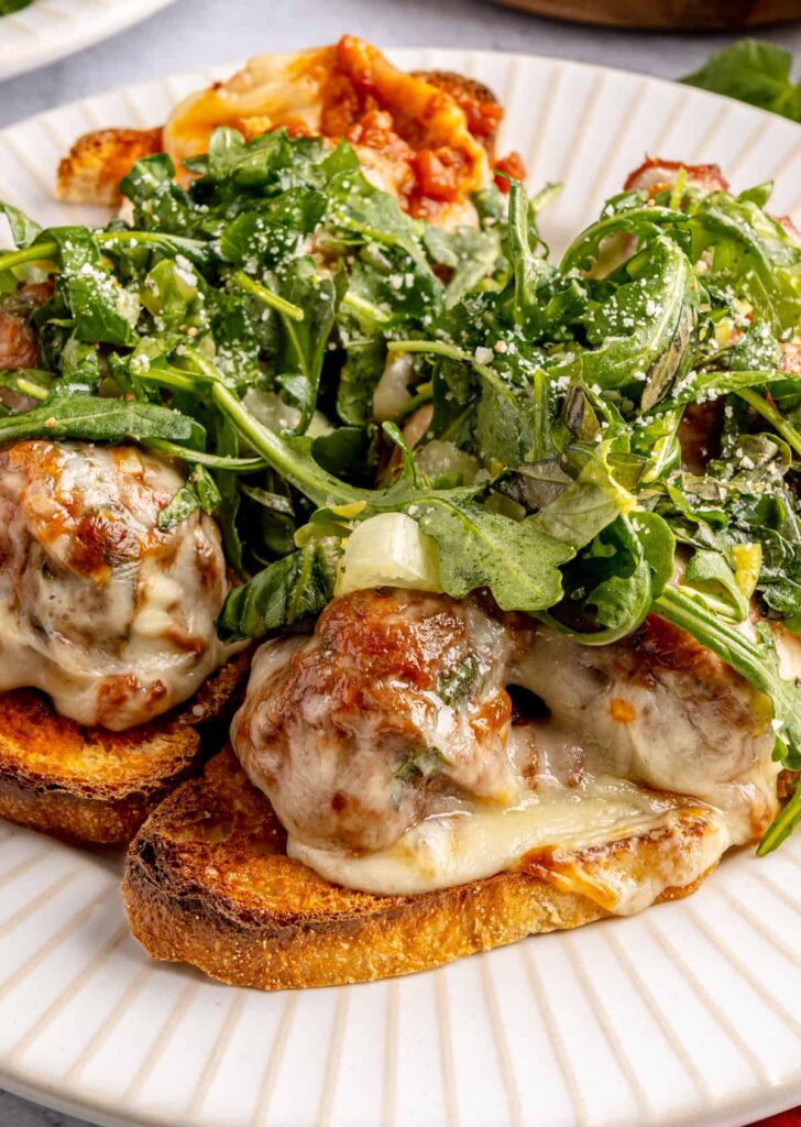 Open-faced, high-protein chicken pesto parmesan meatball subs with marinara sauce and melted cheese