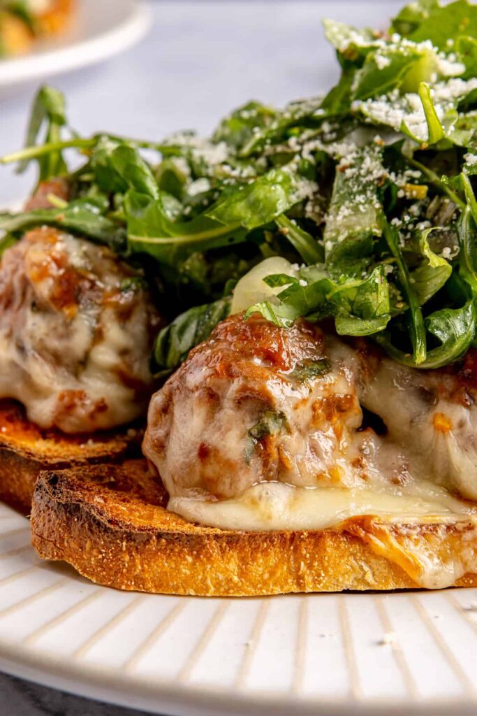 Open-faced, high-protein chicken pesto parmesan meatball subs with marinara sauce and melted cheese