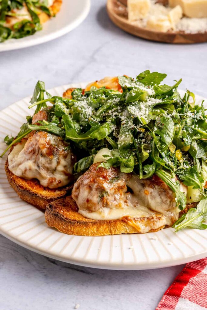 Open-faced, high-protein chicken pesto parmesan meatball subs with marinara sauce and melted cheese